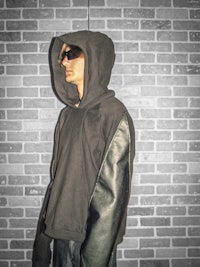 a man in a black hoodie standing in front of a brick wall