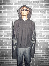 a man in a black hoodie standing against a brick wall